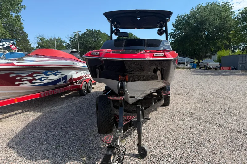 Slide: The Image of 2021 Malibu M220 boat on trailer, parked outdoors, with another boat nearby. - 2