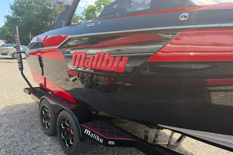 Slide: The Image of 2021 Malibu M220 boat in black and red on a trailer, parked outdoors. - 4
