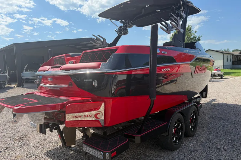 Slide: The Image of 2021 Malibu M220 boat in red and black, featuring Surf Gate technology, parked outdoors. - 5