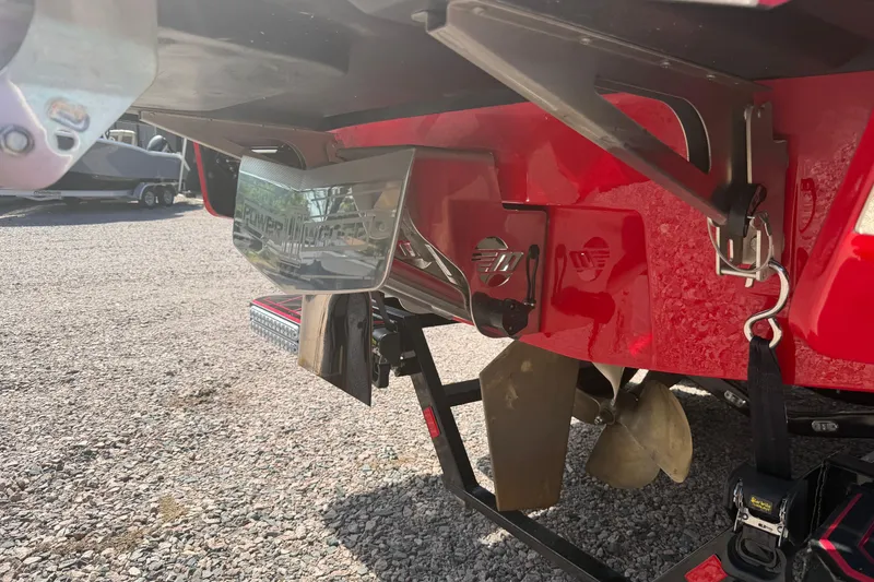 Slide: The Image of 2021 Malibu M220 boat rear view with propeller and Power Wedge, parked on gravel. - 6