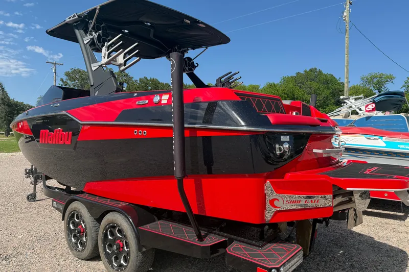 Slide: The Image of 2021 Malibu M220 boat in vibrant red and black, parked on a trailer outdoors. - 9