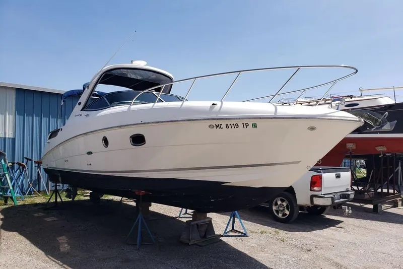 The Image of 2010 Sea Ray Sundancer 310 boat on stands, parked outdoors near a blue building. - 0