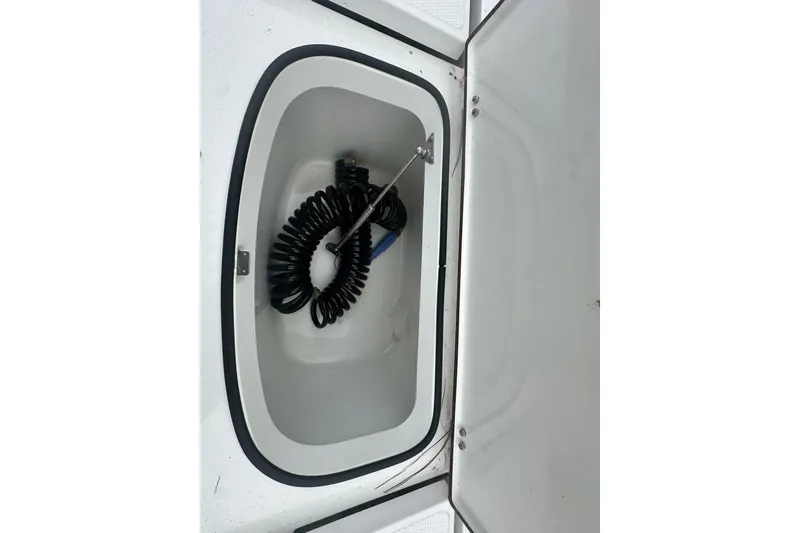Slide: The Image of Open storage compartment on 2022 BlackJack 256 Bay boat with coiled hose inside. - 15
