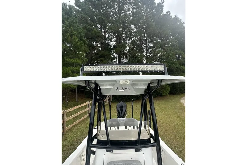 Slide: The Image of 2022 BlackJack 256 Bay boat with T-top and LED light bar, surrounded by trees. - 7