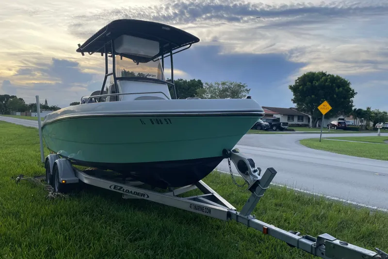 Slide: The Image of 2019 Key Largo 2100 CCW boat on trailer, parked on grass near road. - 2