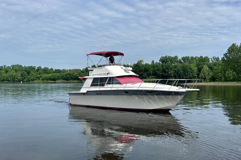 The Image of 1988 Silverton 34 Convertible boat cruising on a calm lake with lush green shoreline. - 0