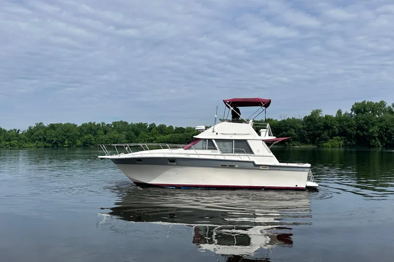 Slide: The Image of 1988 Silverton 34 Convertible boat on calm water with lush green shoreline. - 7