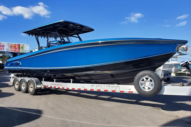 The Image of 2021 Nor-Tech 340 Sport Center Console boat on trailer, vibrant blue and black design. - 0