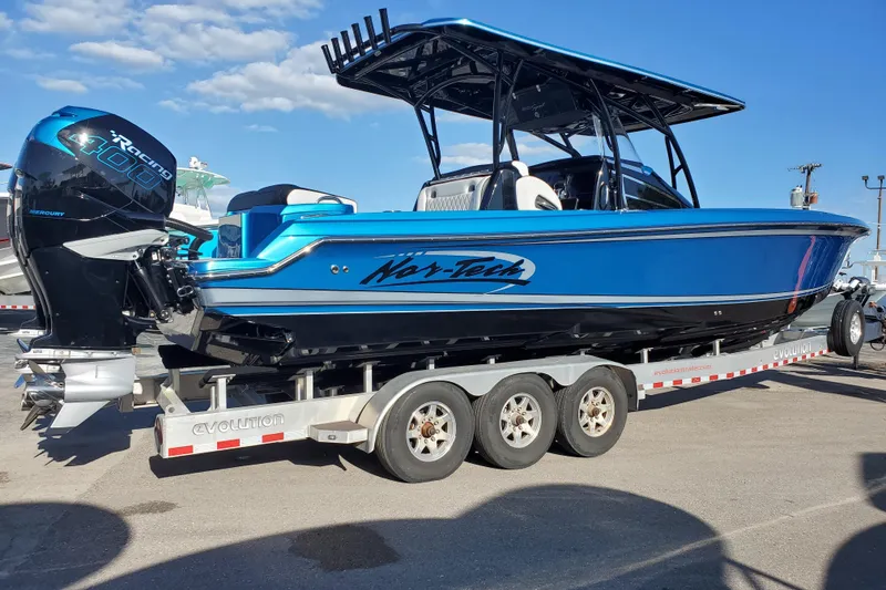 Slide: The Image of 2021 Nor-Tech 340 Sport Center Console boat on trailer, featuring vibrant blue design. - 2