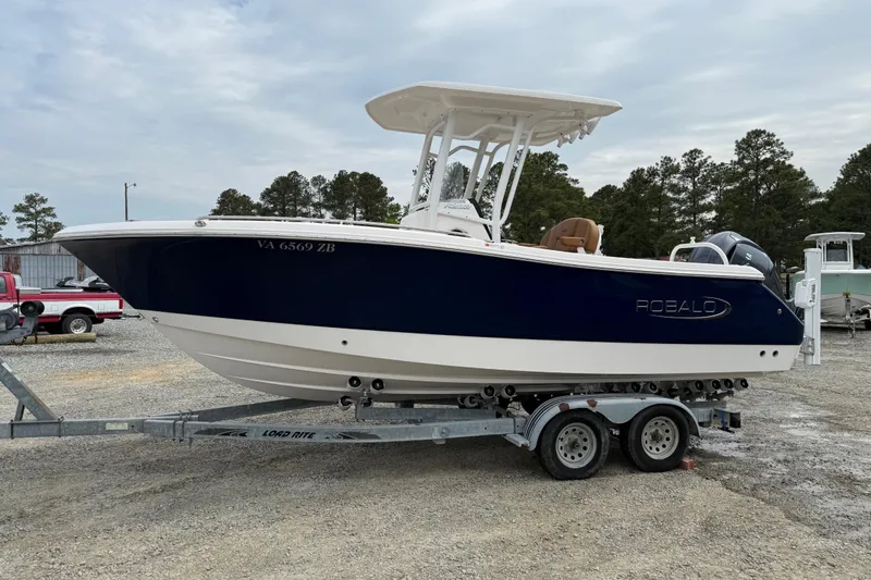 Slide: The Image of 2025 Robalo R232 Explorer boat on trailer, parked outdoors, with trees in the background. - 15