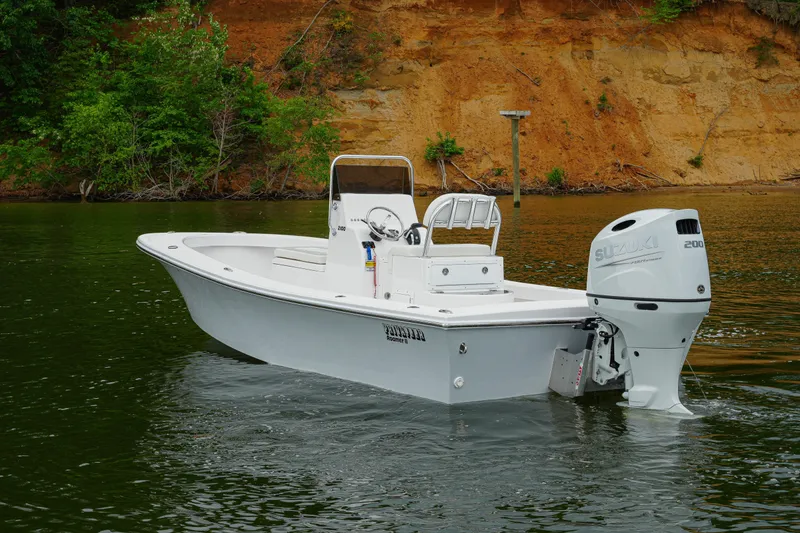 Slide: The Image of 2026 Privateer 2100 Roamer boat with Suzuki engine on calm water near a rocky shoreline. - 1