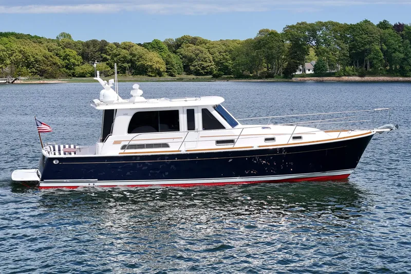 Slide: The Image of 2015 Sabre 42 Salon Express yacht cruising on a serene lake with lush green shoreline. - 2