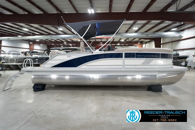 Slide: The Image of 2026 Bennington 22 ML pontoon boat in indoor showroom with canopy and sleek design. - 6
