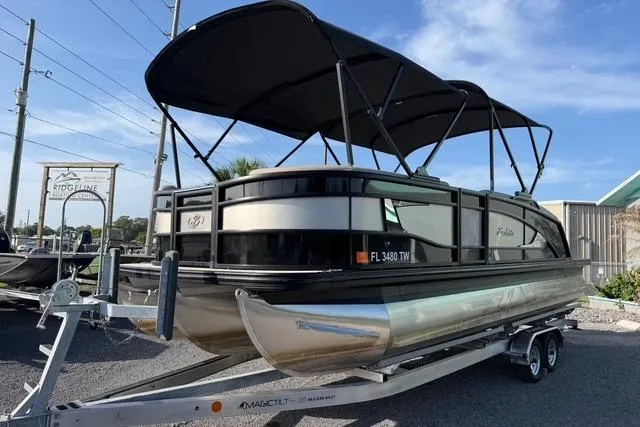 The Image of 2023 Barletta L23U pontoon boat on trailer with black canopy, parked outdoors. - 1