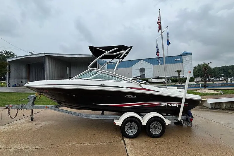 Slide: The Image of 2011 Sea Ray 205 Sport boat on trailer, parked near marina under cloudy sky. - 4