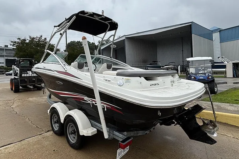 Slide: The Image of 2011 Sea Ray 205 Sport boat on trailer, parked outdoors near industrial buildings. - 5