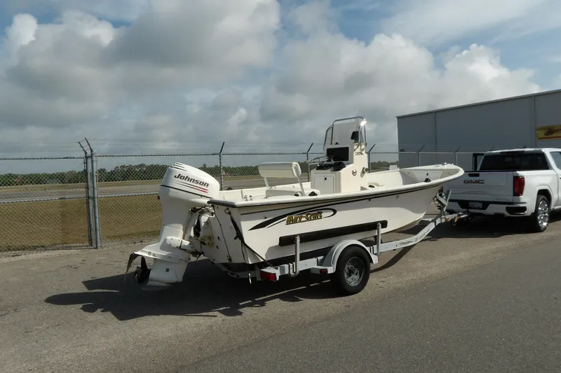 Slide: The Image of 2005 May-Craft 1800 Skiff boat on trailer, with Johnson outboard motor, parked near a fence. - 1
