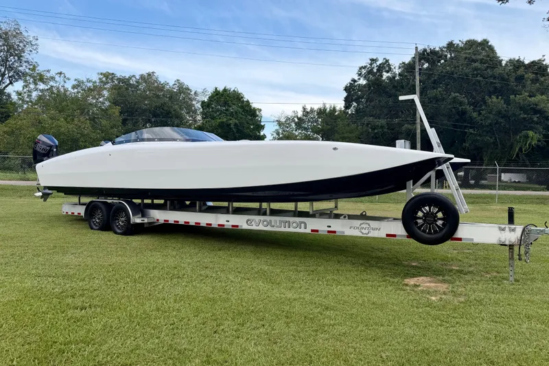Slide: The Image of 2024 Fountain 34 Thundercat boat on trailer, parked on grass, with trees in background. - 21