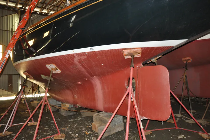 Slide: The Image of 1970 Hinckley Bermuda 40 sailboat in dry dock, supported by stands, showcasing its hull. - 7