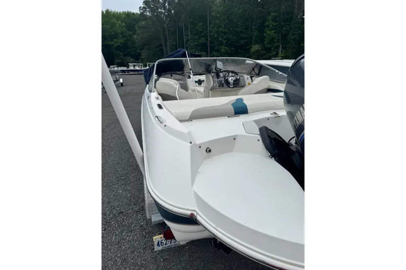 Slide: The Image of 2013 Stingray 204 LR boat with white interior, parked outdoors near trees. - 2