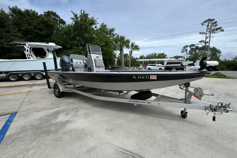 Slide: The Image of 2021 Avid 21 FS boat on trailer in parking lot, surrounded by trees and vehicles. - 7