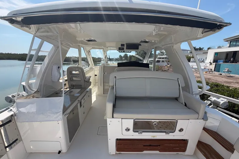 Slide: The Image of 2022 Boston Whaler 380 Realm interior with seating and helm, docked by waterfront homes. - 3