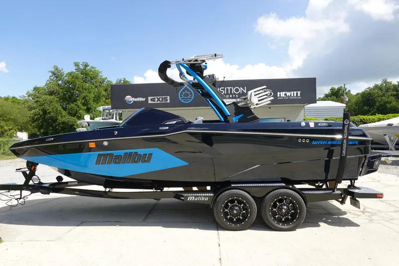 The Image of 2024 Malibu Wakesetter 23 MXZ boat on trailer, black and blue design, sunny day. - 1