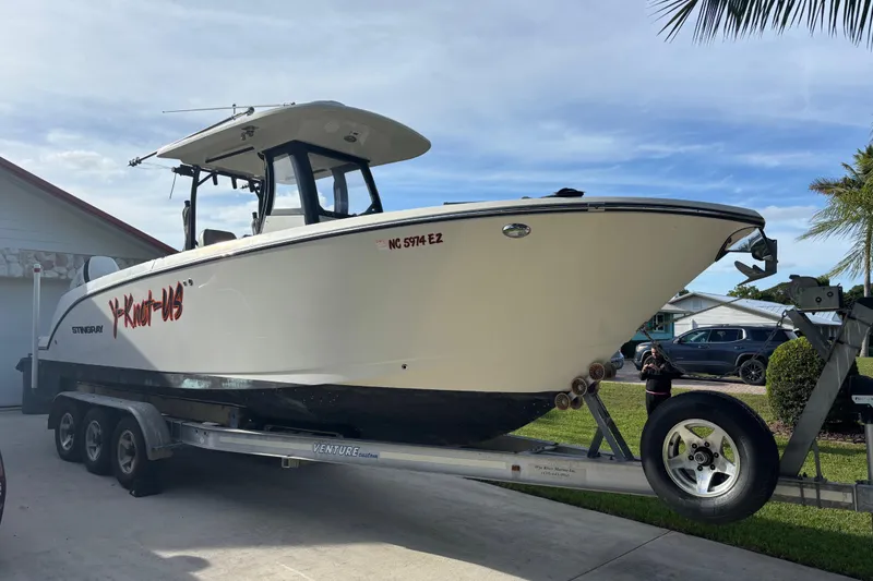 The Image of 2023 Stingray 273 CC boat on trailer, parked in driveway under clear sky. - 0