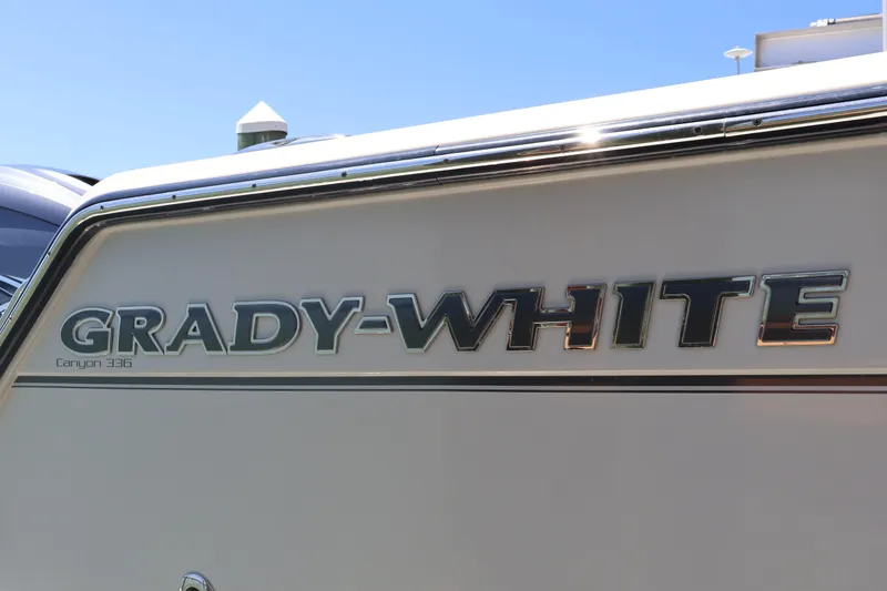Slide: The Image of 2021 Grady-White Canyon 336 boat logo on hull under clear blue sky. - 18
