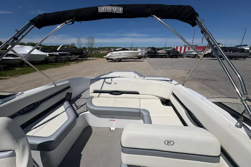 Slide: The Image of 2021 Cobalt CS23 boat interior with white seating and canopy, parked outdoors. - 6