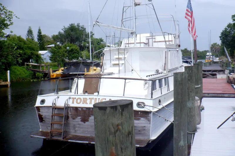 Slide: The Image of 1980 Grand Banks 49 Classic yacht docked, displaying American flag, lush greenery in background. - 2