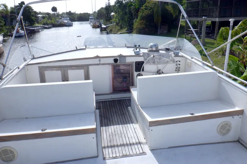 Slide: The Image of 1980 Grand Banks 49 Classic yacht deck with seating and steering wheel, overlooking a serene waterway. - 4