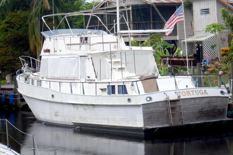 Slide: The Image of 1980 Grand Banks 49 Classic yacht named "Tortuga" docked by a lush, tropical setting. - 59