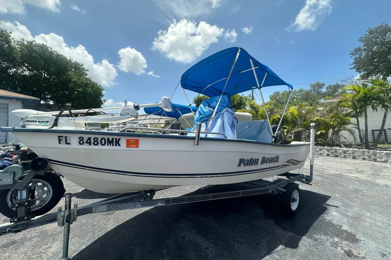 The Image of 2004 Palm Beach 161 Whitecap boat with blue canopy on trailer, parked outdoors. - 0