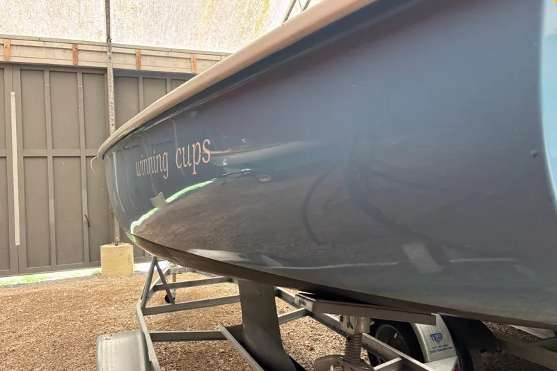Slide: The Image of 1971 Rhodes 19 sailboat with "winning cups" text on hull, stored indoors. - 2