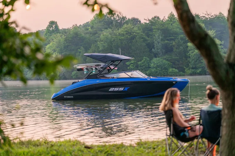 Slide: The Image of 2026 Yamaha Boats 255XD on a serene lake with people relaxing nearby. - 2