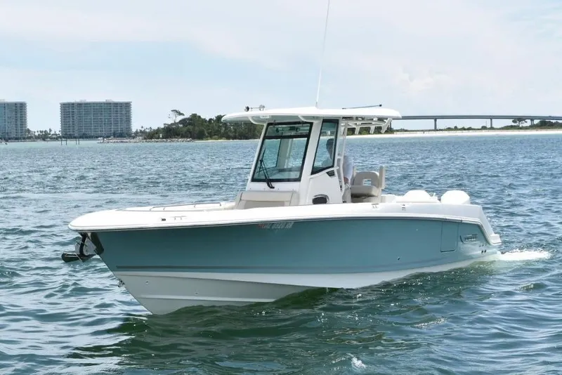 Slide: The Image of 2023 Boston Whaler 280 Outrage boat cruising on open water, with coastal buildings in the background. - 2
