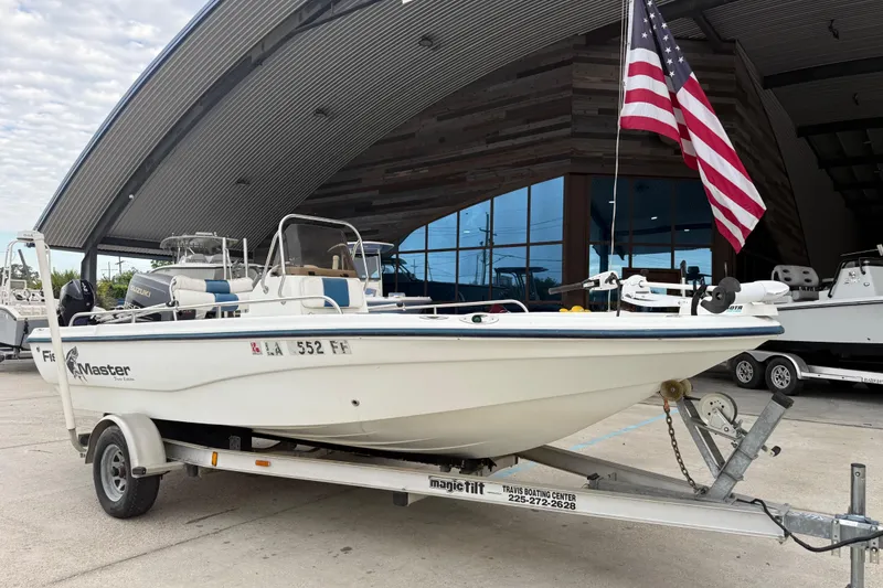 Slide: The Image of 2002 Fishmaster 19 boat on trailer with American flag, parked outside a modern building. - 3
