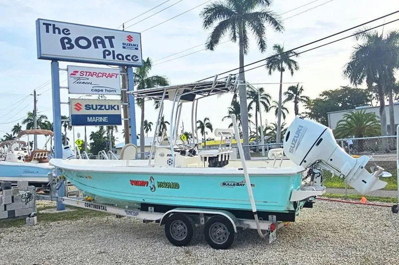 The Image of 2023 Bulls Bay 2200 boat with Suzuki engine at dealership, surrounded by palm trees. - 0
