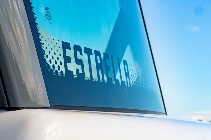 Slide: The Image of Close-up of 2027 HCB 65 Estrella boat window with logo and blue sky background. - 63