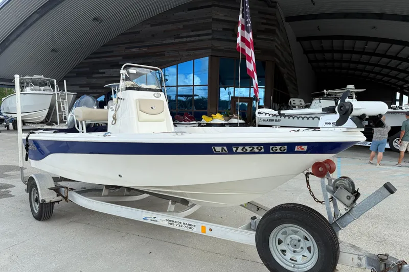 Slide: The Image of 2017 NauticStar 1910 NauticBay boat on trailer, displayed outdoors with American flag. - 2