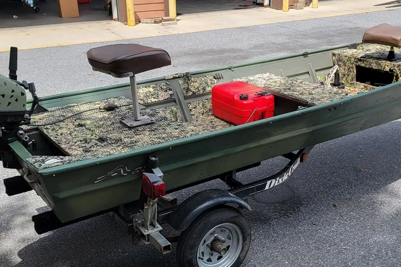 The Image of 1994 Alumacraft 1436 Jon boat on trailer, featuring camouflage interior and red fuel tank. - 0