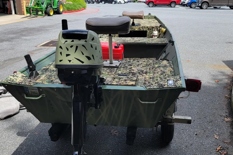 Slide: The Image of 1994 Alumacraft 1436 Jon boat with camouflage interior and outboard motor in a parking lot. - 6