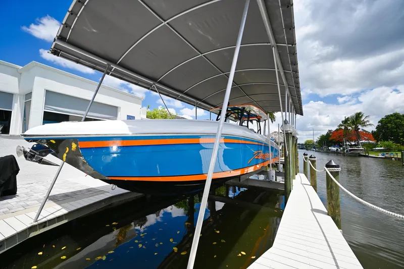 Slide: The Image of 2027 Renegade 38' Open boat on lift, vibrant blue and orange design, docked by a canal. - 26
