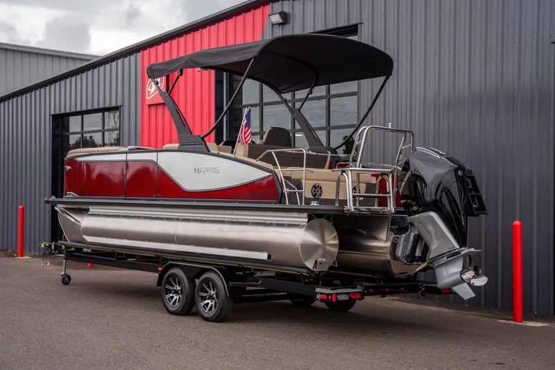 Slide: The Image of 2026 Harris Sunliner 230 pontoon boat on trailer, parked outside a modern building. - 12