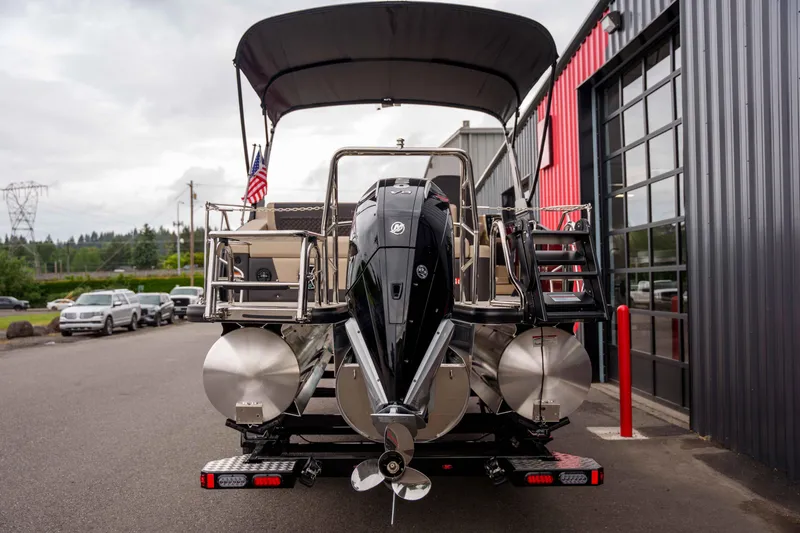 Slide: The Image of 2026 Harris Sunliner 230 pontoon boat with outboard motor, parked near a modern building. - 13