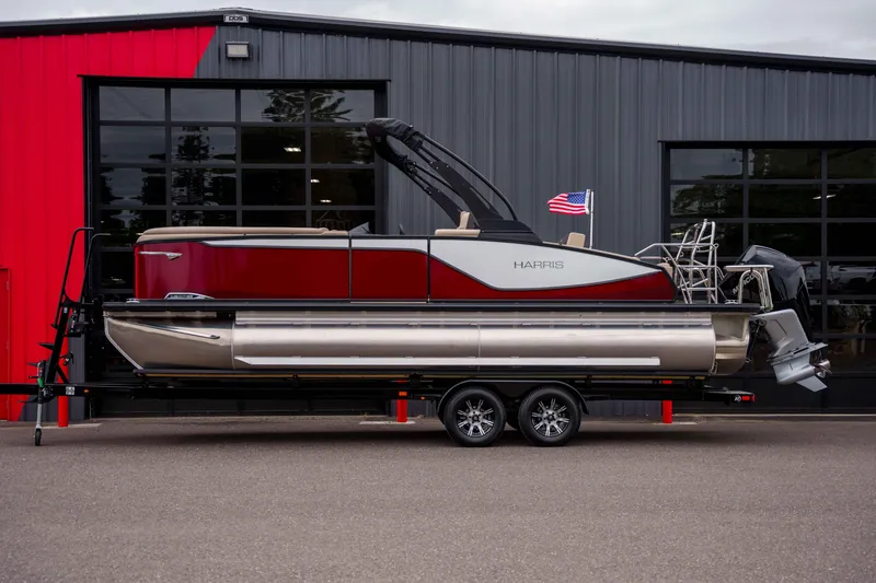 Slide: The Image of 2026 Harris Sunliner 230 pontoon boat on trailer, parked outside a modern building. - 14