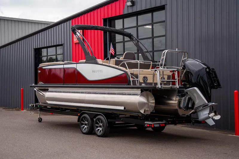 Slide: The Image of 2026 Harris Sunliner 230 pontoon boat on trailer, parked outside a modern building. - 17