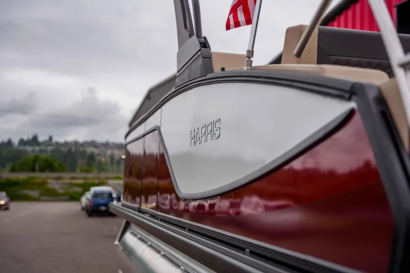 Slide: The Image of 2026 Harris Sunliner 230 pontoon boat with American flag, parked outdoors. - 43