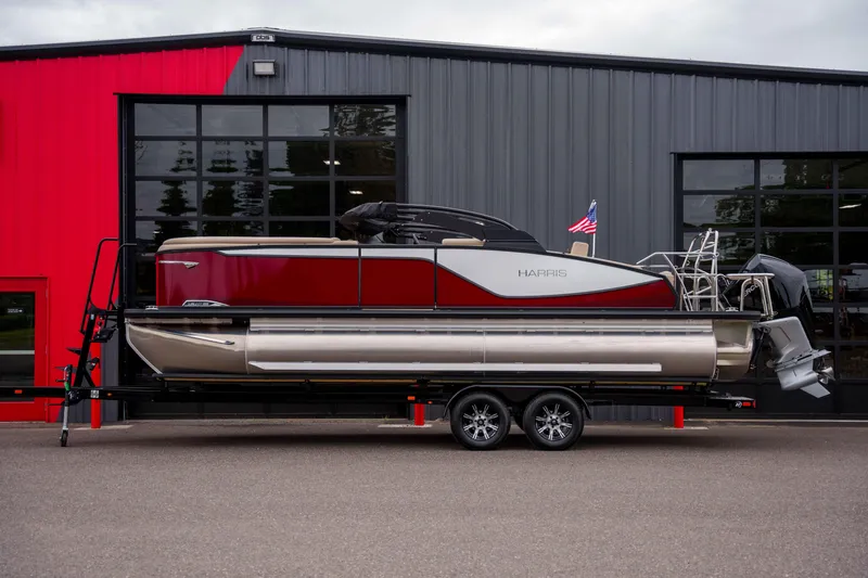 Slide: The Image of 2026 Harris Sunliner 230 pontoon boat on trailer, parked outside a modern building. - 48